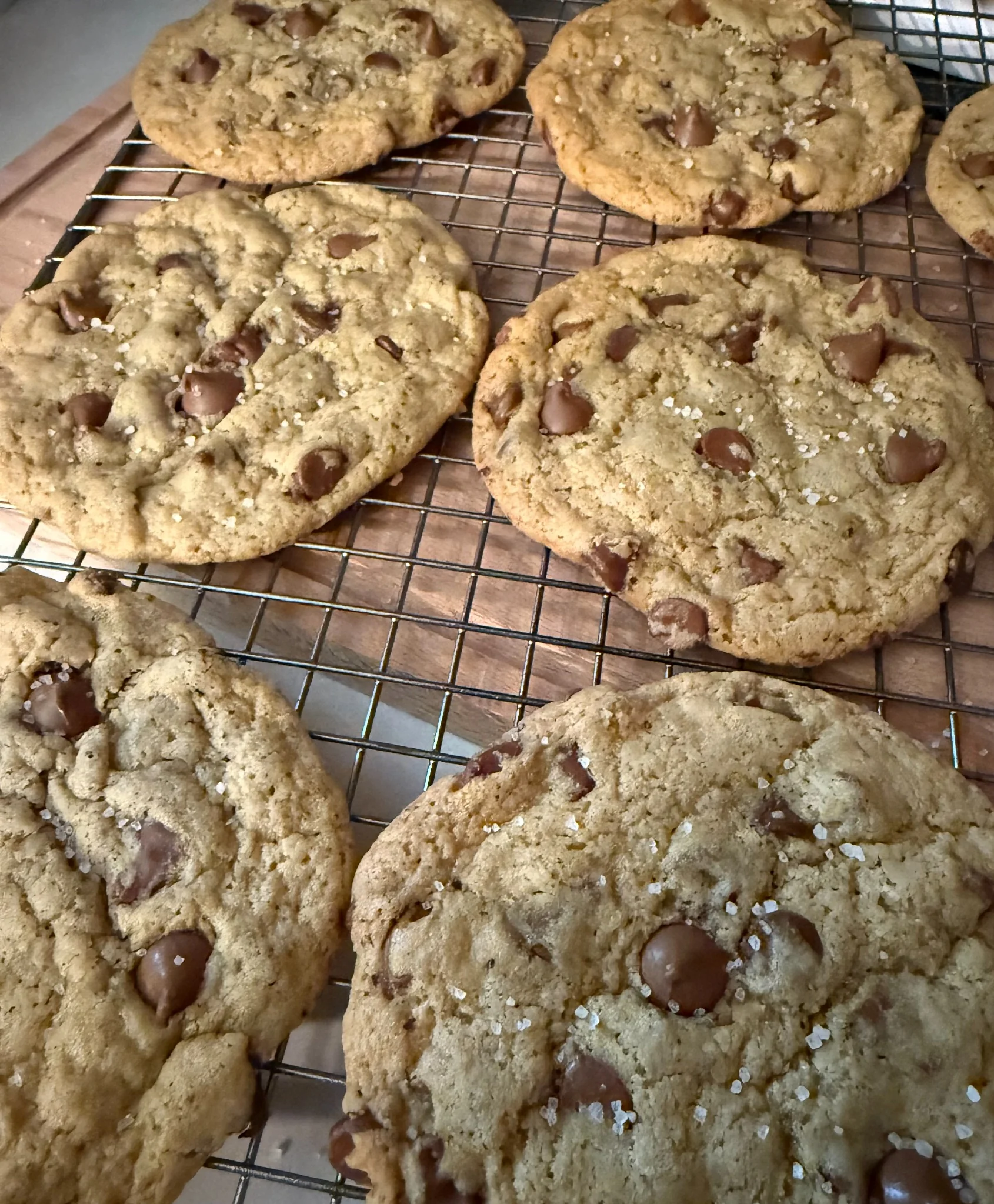 A stack of thick chocolate chip cookies with flaky sea salt on a cooling rack