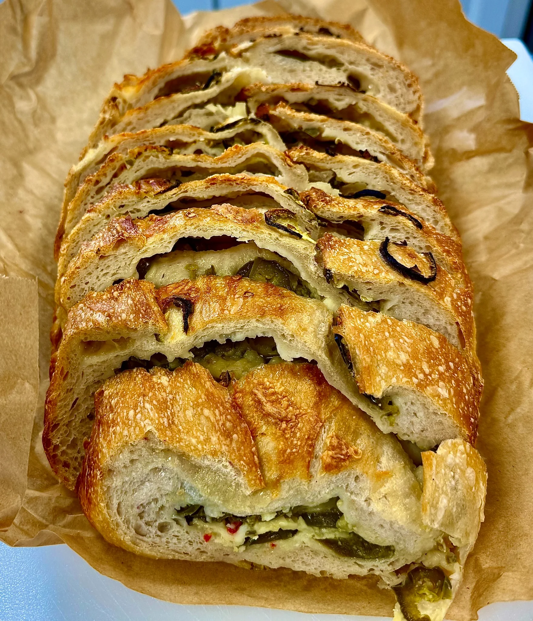 A sliced sourdough loaf on parchment showing an open, glossy crumb, with a dish of salted butter