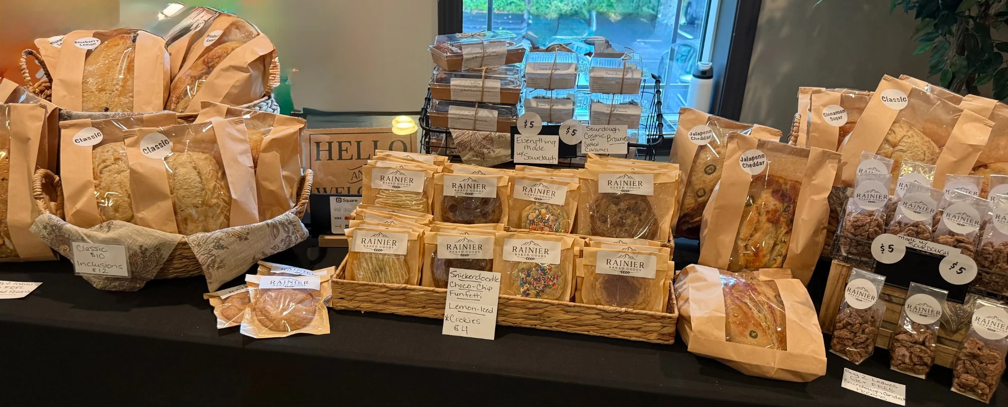 A bakery market stall with baskets of sourdough loaves and paper-wrapped cookies under a canvas canopy in morning light
